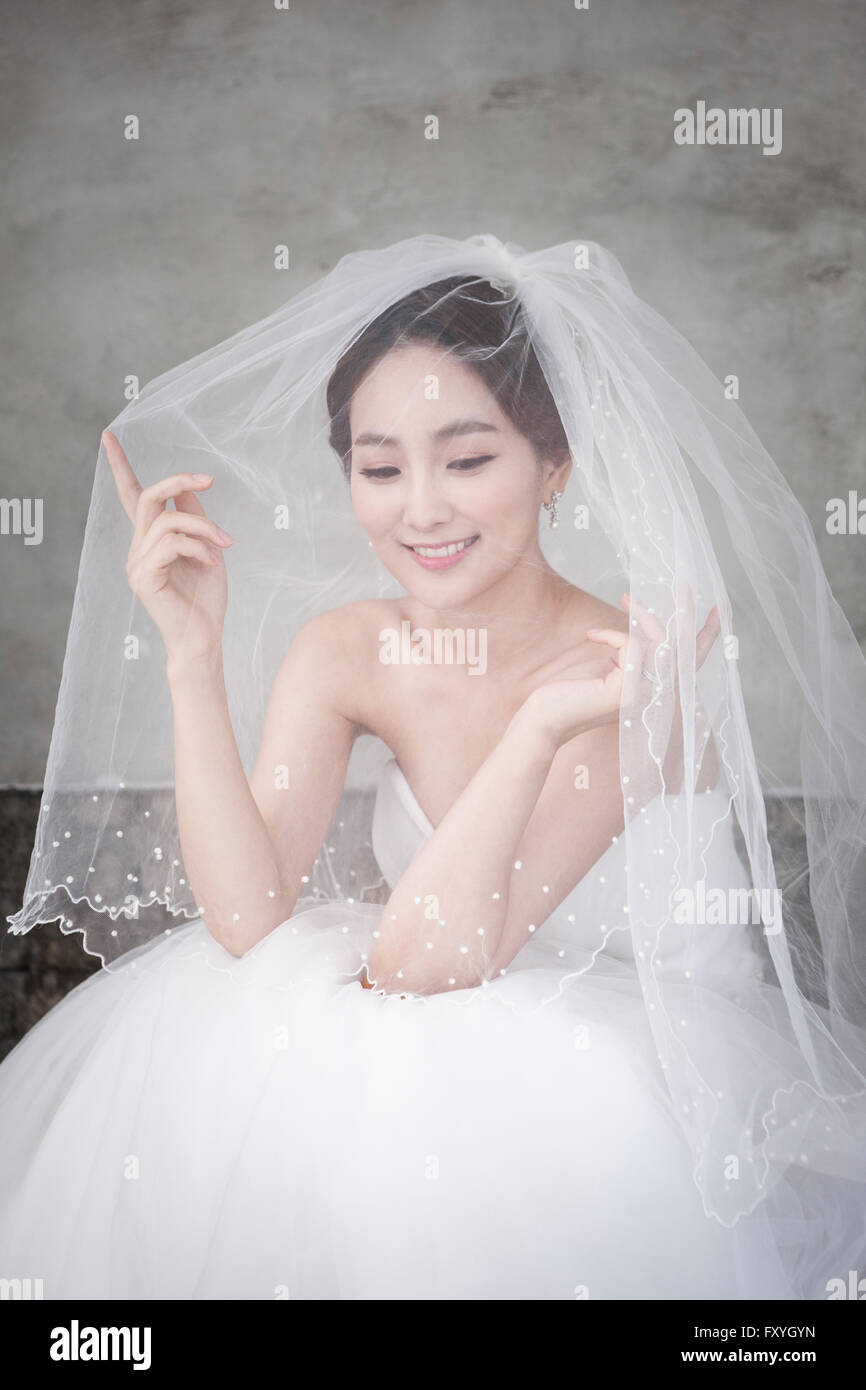 Braut unter Hochzeitsschleier mit Handbewegung nach unten mit einem Lächeln Stockfoto