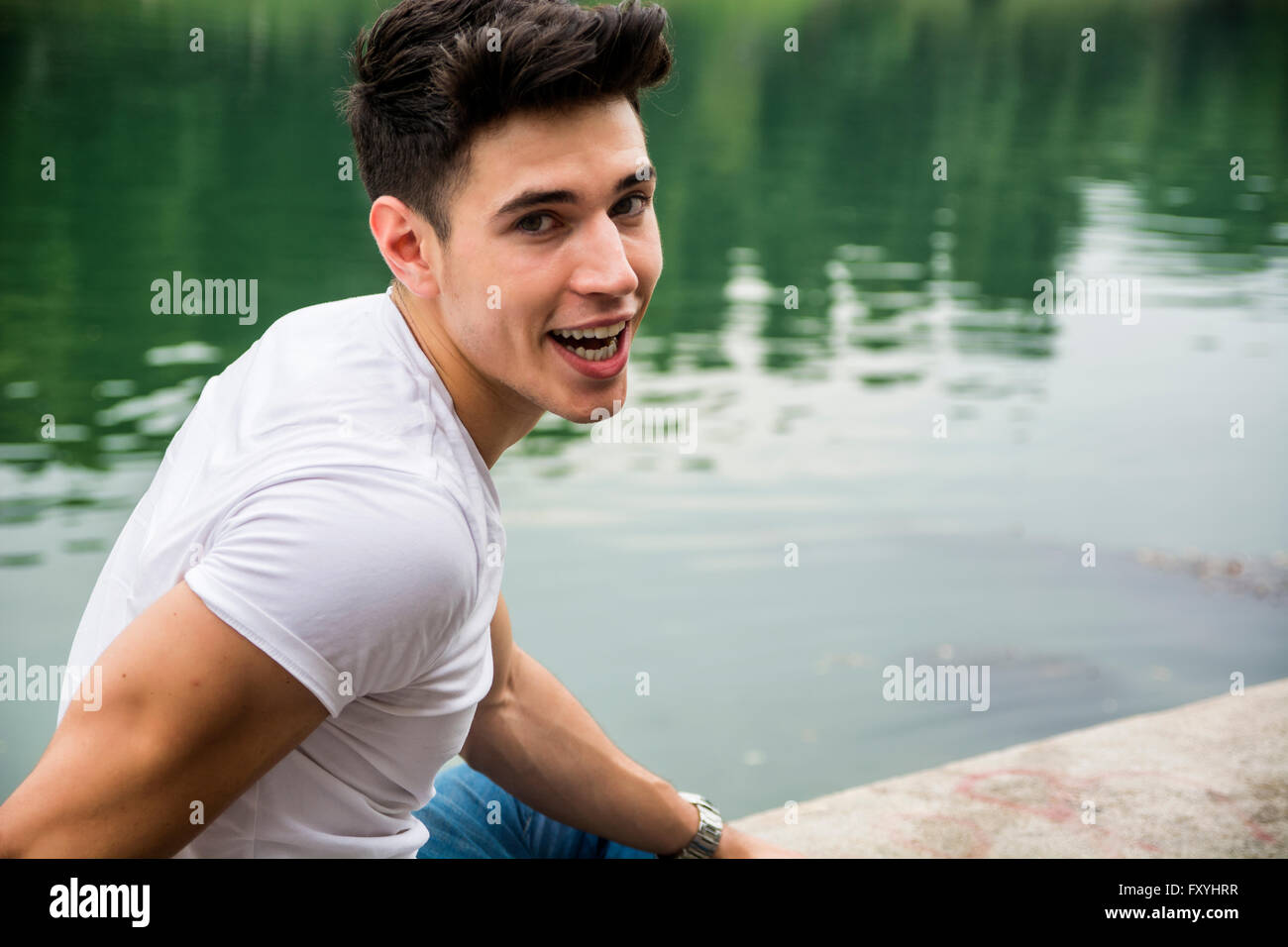 Jovial dunkelhaarige junge Mann lächelnd in die Kamera gegen Wasser Stockfoto