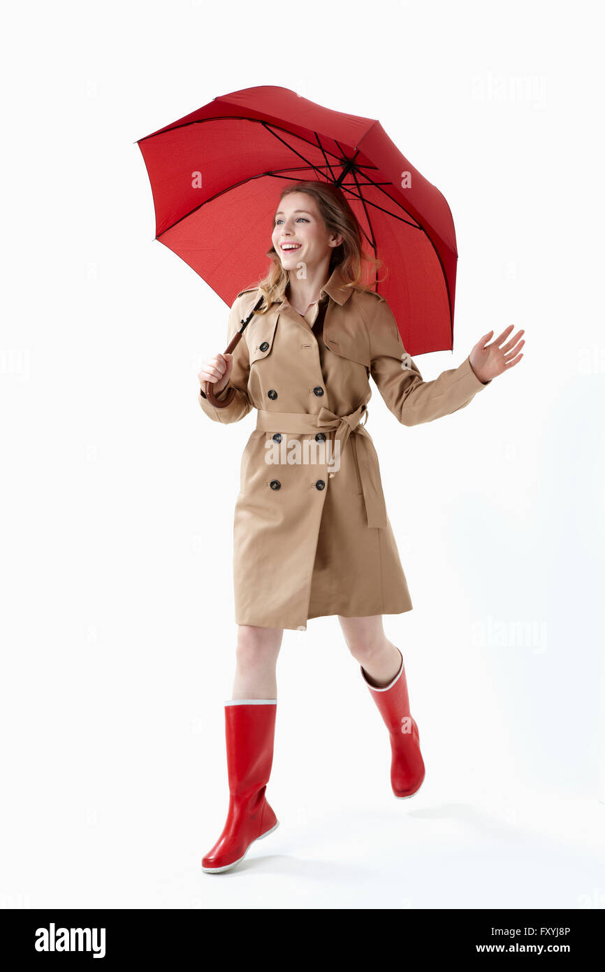 Frau im Trenchcoat und roten Regen Stiefel halten einen roten Regenschirm und Wandern Stockfoto
