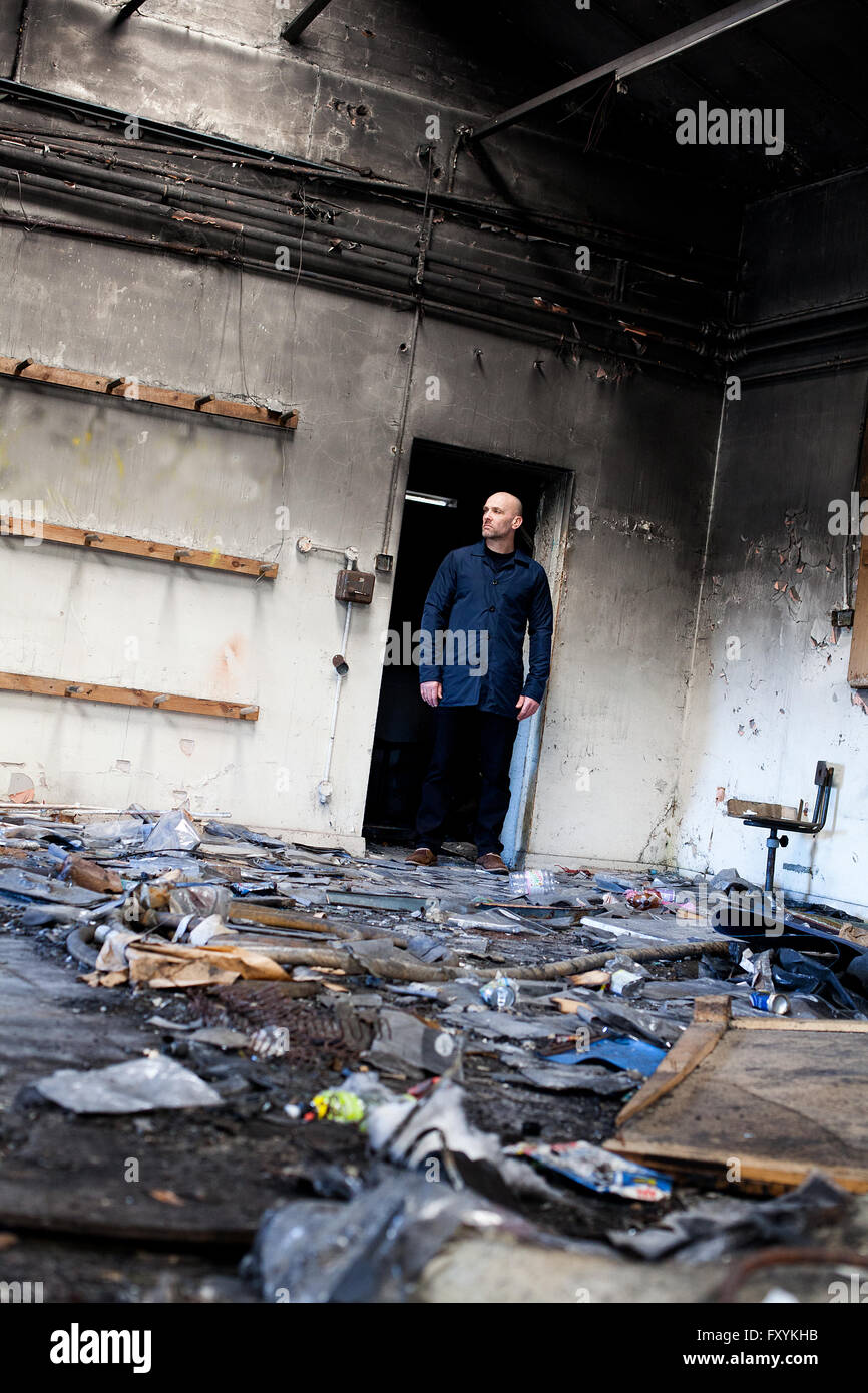 Mann, der in einer Tür ein verlassener Gebäude mit viel Schutt und Müll auf dem Boden Stockfoto