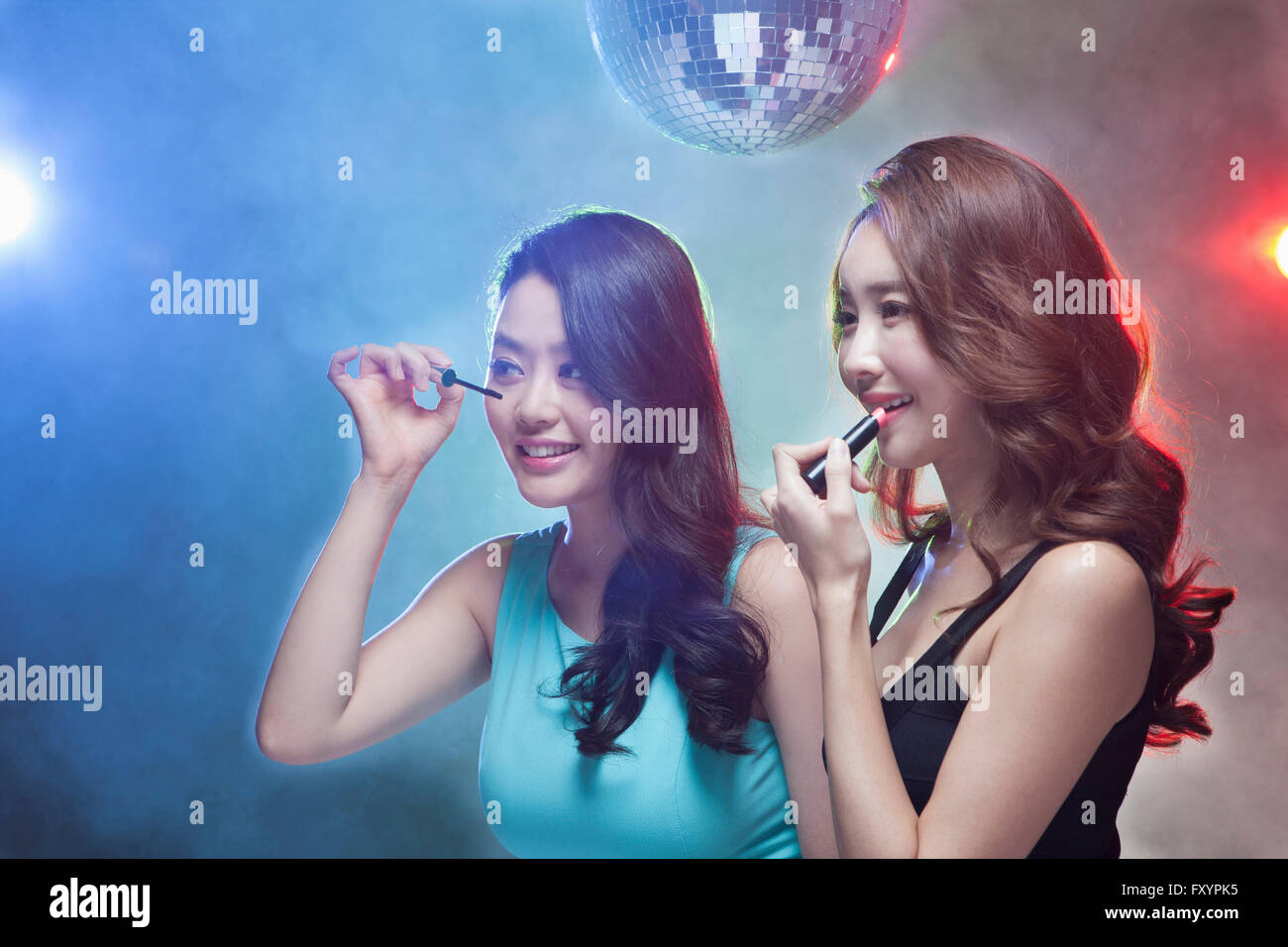 Seitenansicht zweier junger lächelnde Frauen setzen auf Make-up im Nachtclub Stockfoto