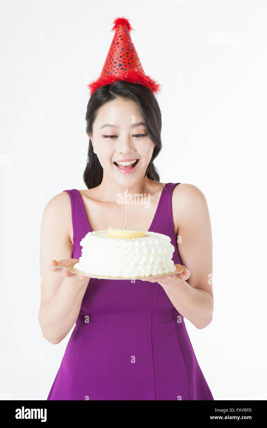 Porträt des jungen lächelnde Frau mit Partyhut hält einen Kuchen nach unten Stockfoto