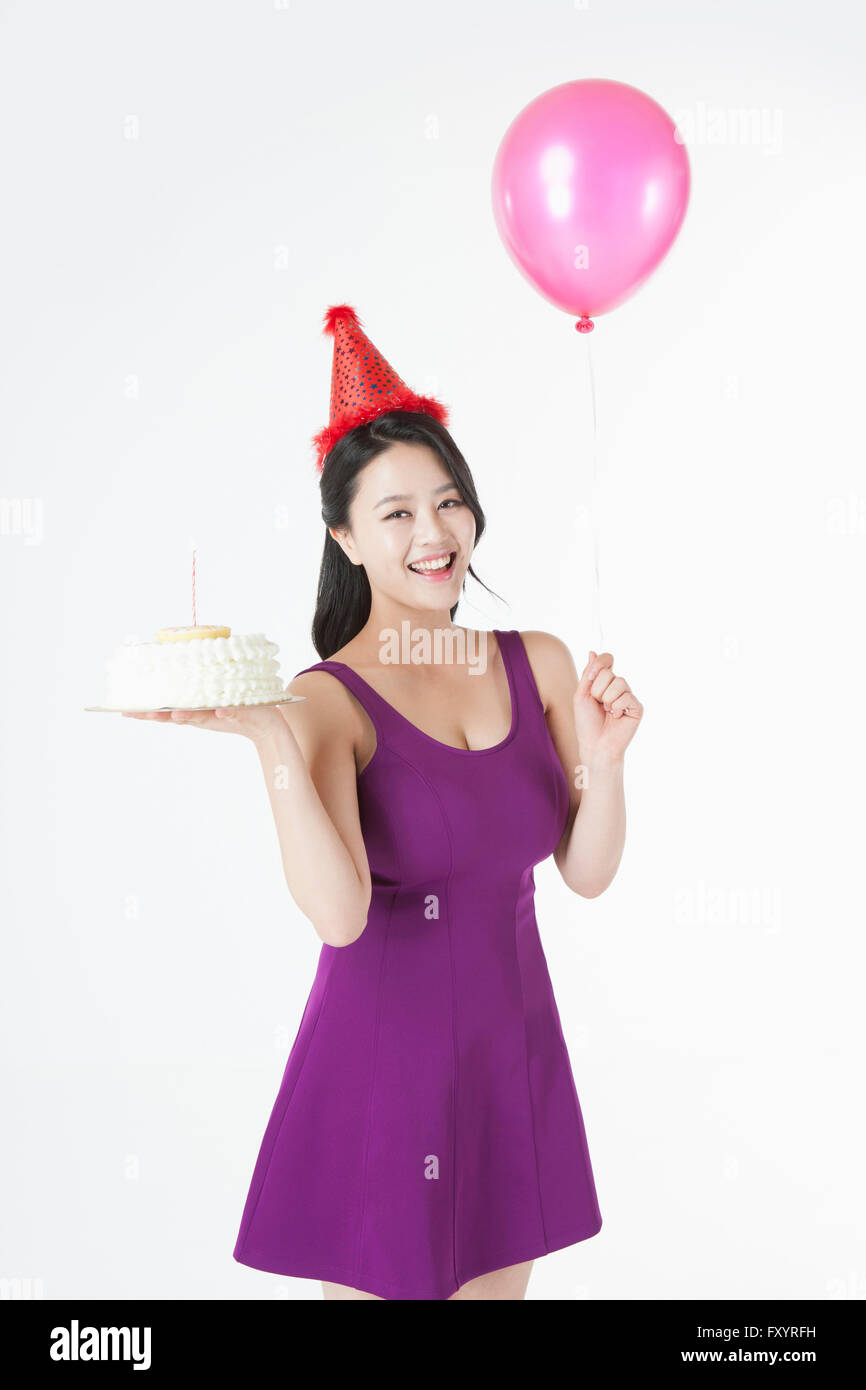 Junge lächelnde Frau mit Partyhut hält einen Kuchen und ein Ballon Stockfoto