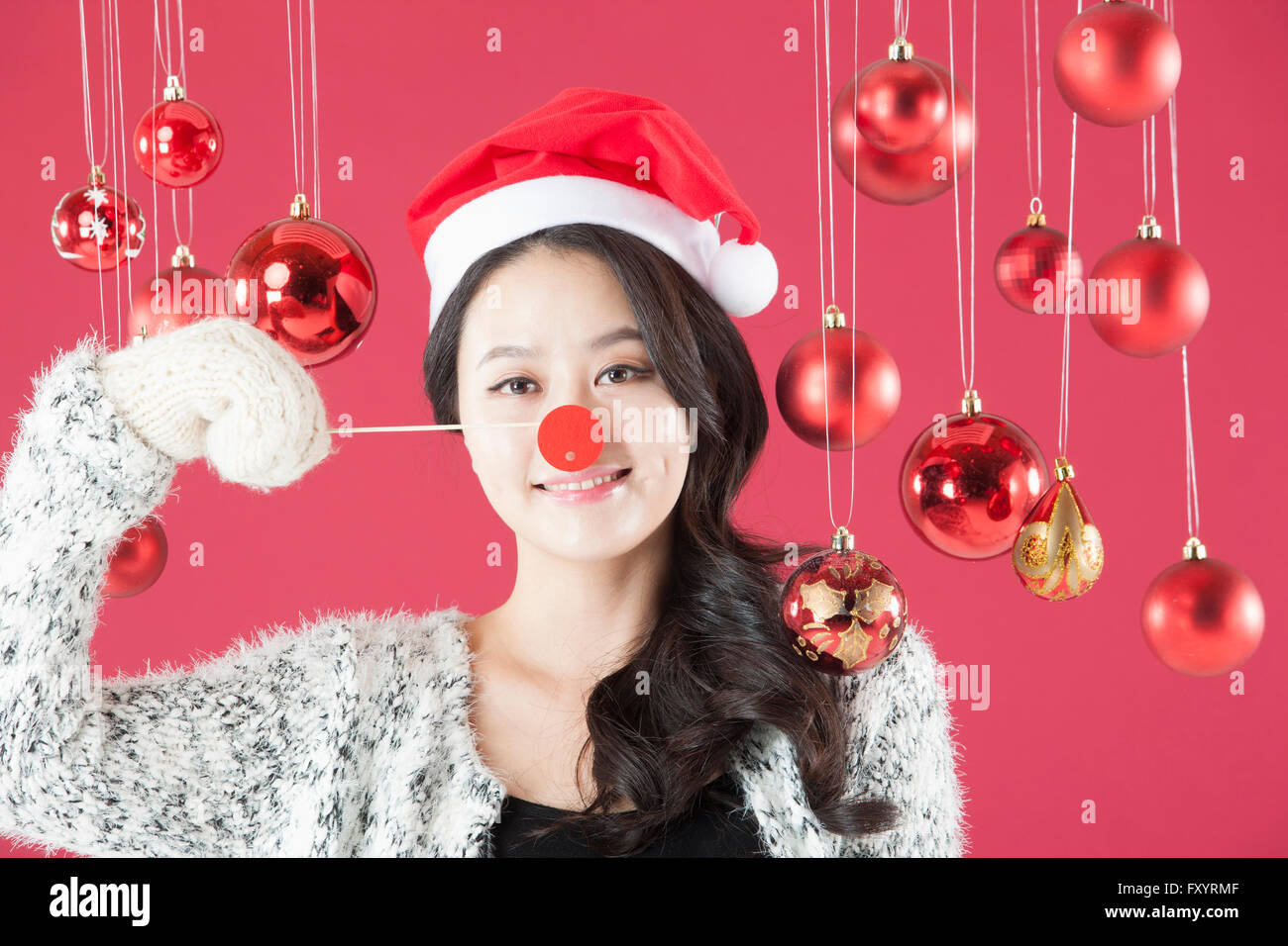 Porträt des jungen lächelnde Frau mit Santa Hut und Nase von Reh und starrte auf Vorderseite mit Weihnachtskugeln Stockfoto