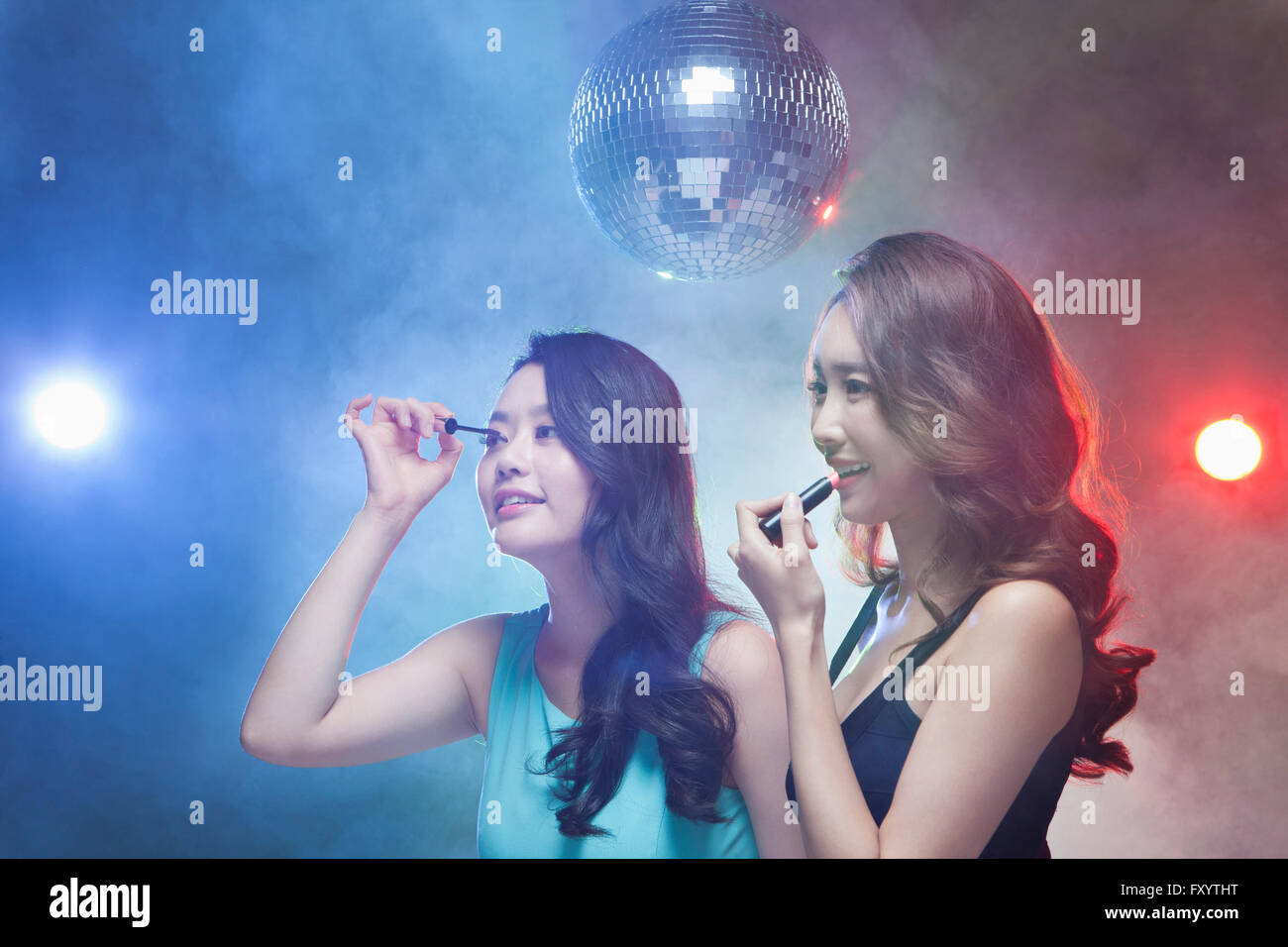 Seite Ansicht Porträt von zwei jungen Frauen setzen auf Wimperntusche und Lippenstift im Nachtclub lächelnd Stockfoto