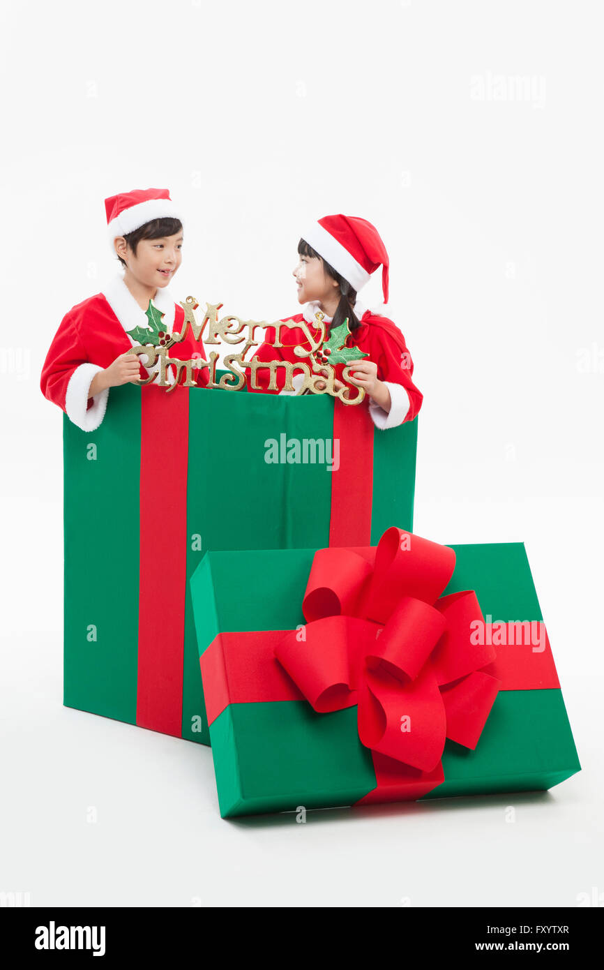 Lächelnde junge und Gril in Santas Kleidung in Geschenkbox mit Weihnachtsdekoration von Angesicht zu Angesicht Stockfoto