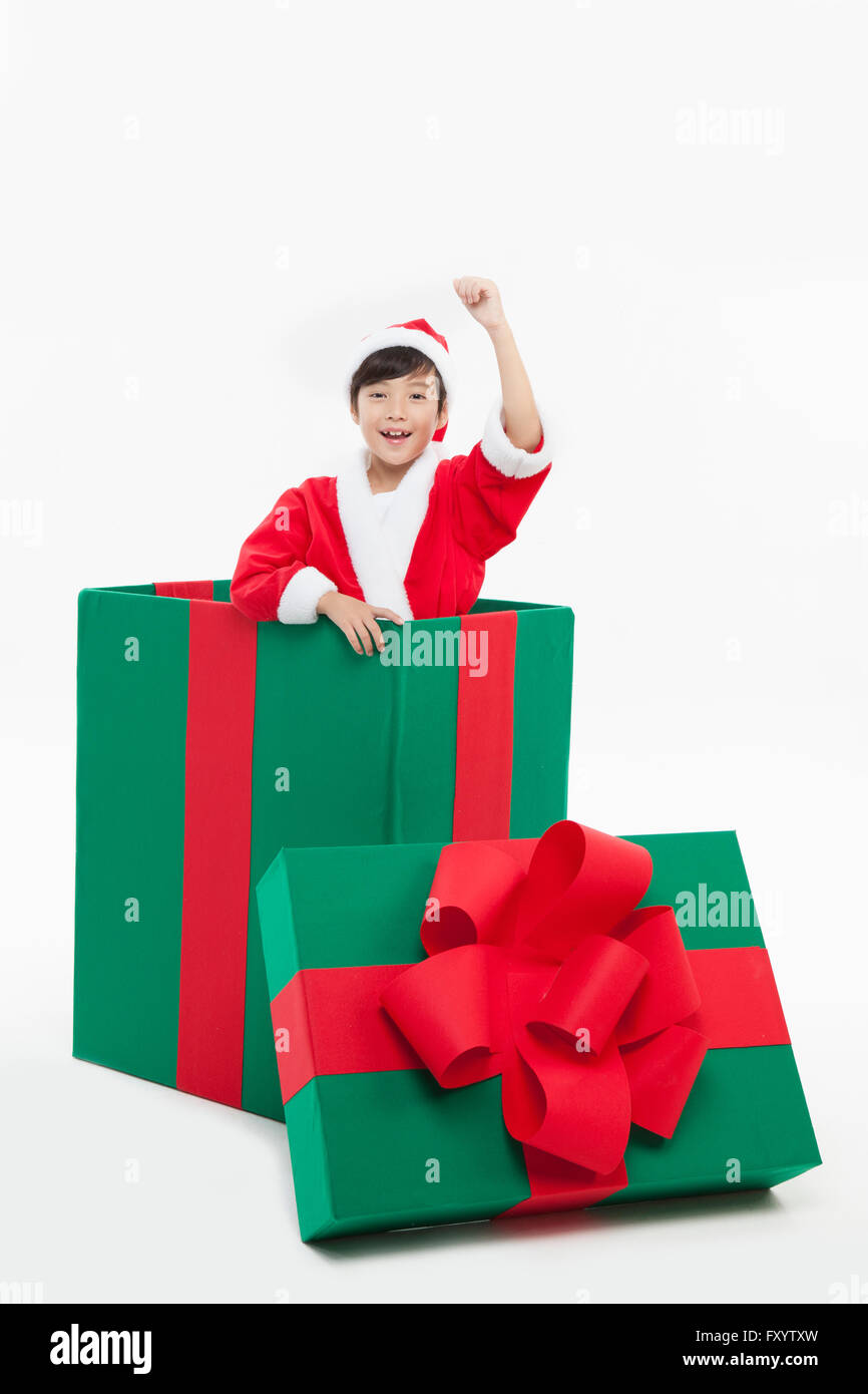 Lächelnde junge in Santas Kleidung mit Arm in eine große Geschenkbox starrte auf Vorderseite Stockfoto