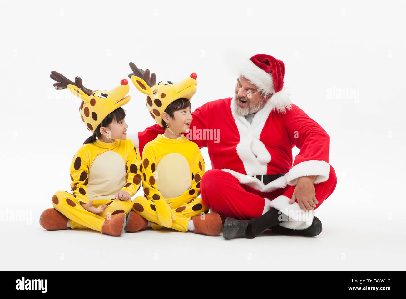 Lächelnde Kinder gekleidet wie Hirsche und Weihnachtsmann Gesicht sitzen Stockfoto