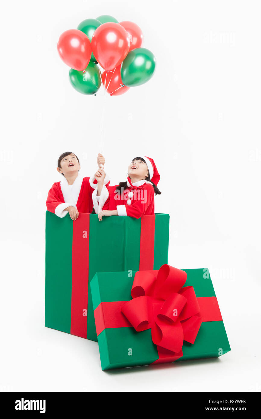 Porträt der jungen und Mädchen in Santas Kleidung mit Ballons in eine große Geschenkbox nachschlagen Stockfoto