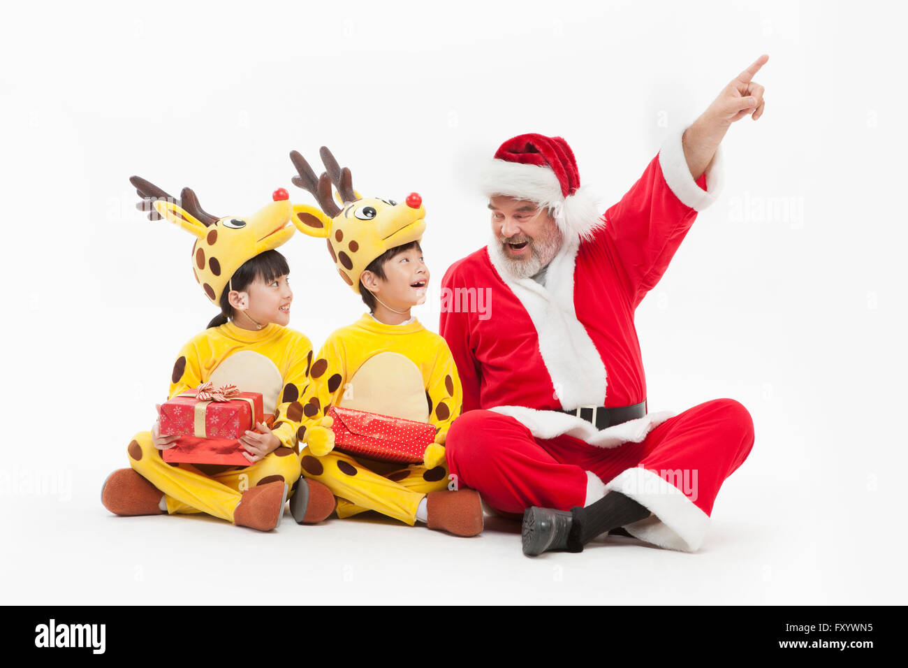 Lächelnde Kinder gekleidet wie Rentiere und lächelnde Santa sitzen auf etwas von Angesicht zu Angesicht Stockfoto