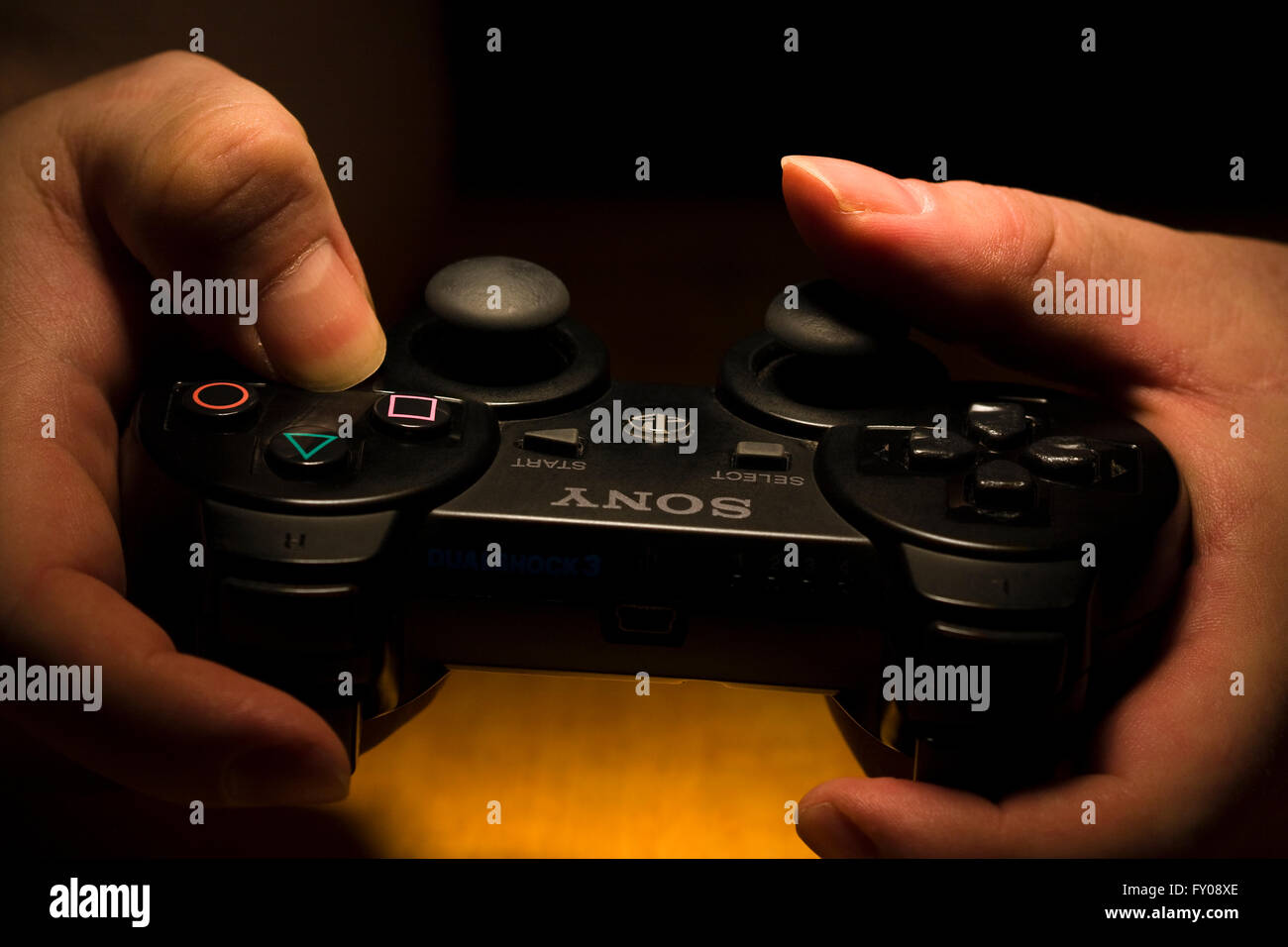 Zwei Hände halten ein drahtloses SONY Playstation Dual Shock 3 Controller, während der Daumen die Tasten bearbeiten Stockfoto