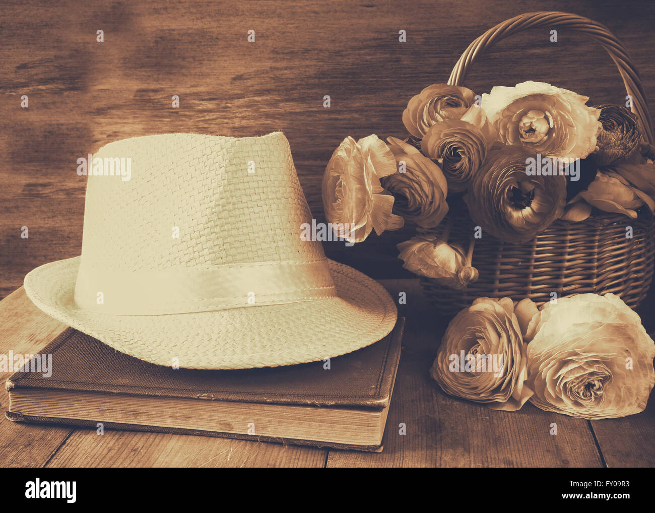 Fedora-Hut neben altes Buch und Blumen auf Holztisch. Sepia Jahrgang gefiltert Stockfoto