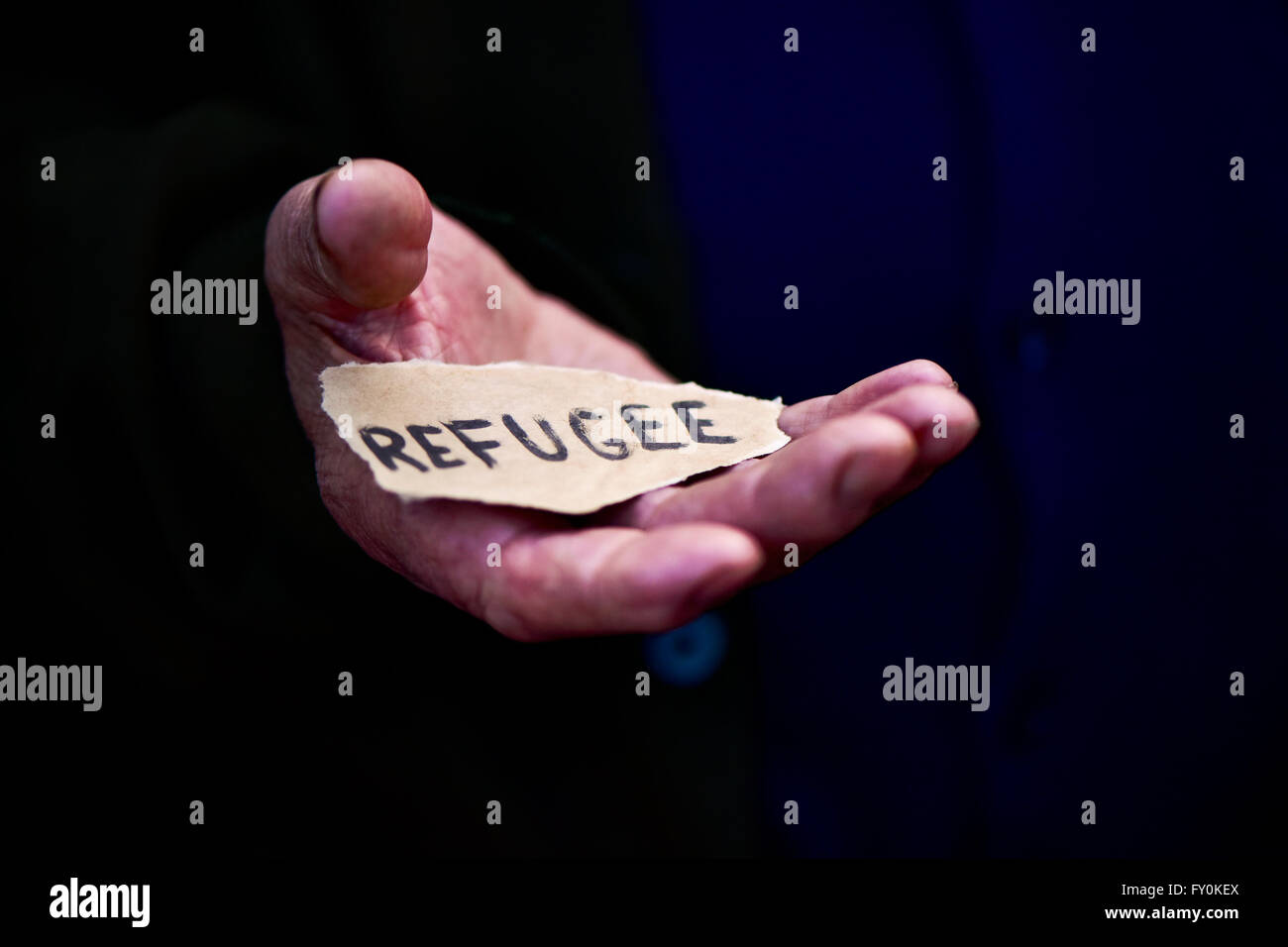 Nahaufnahme der Hand eines alten Mannes mit einem Stück Papier mit dem Wort Flüchtling mit einen dramatischen Effekt Stockfoto