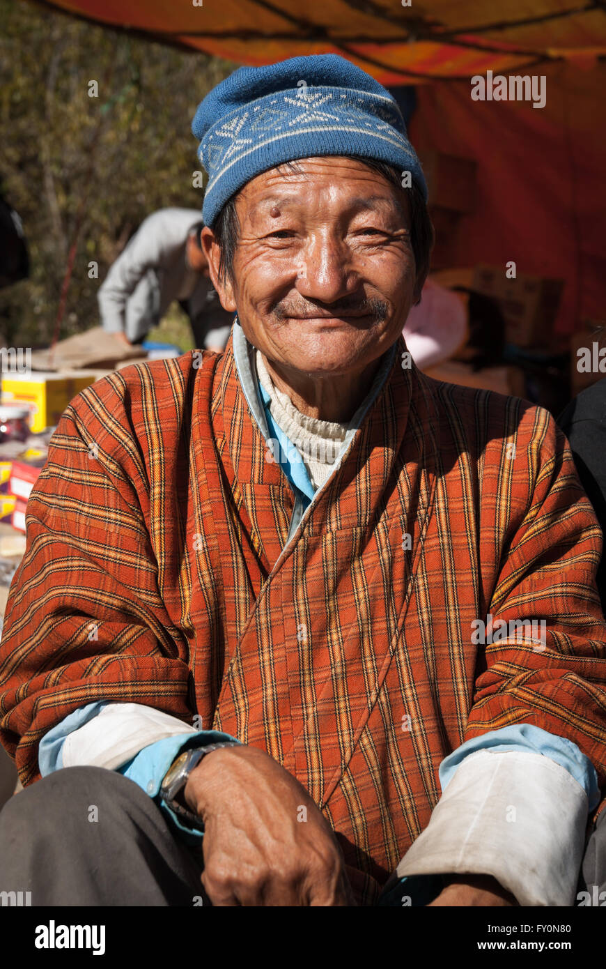 Porträt von älteren bhutanischen Mann tragen traditionelle Gho in seinem Stall in den Wochenendmarkt Gemüse in Thimphu, Bhutan Stockfoto