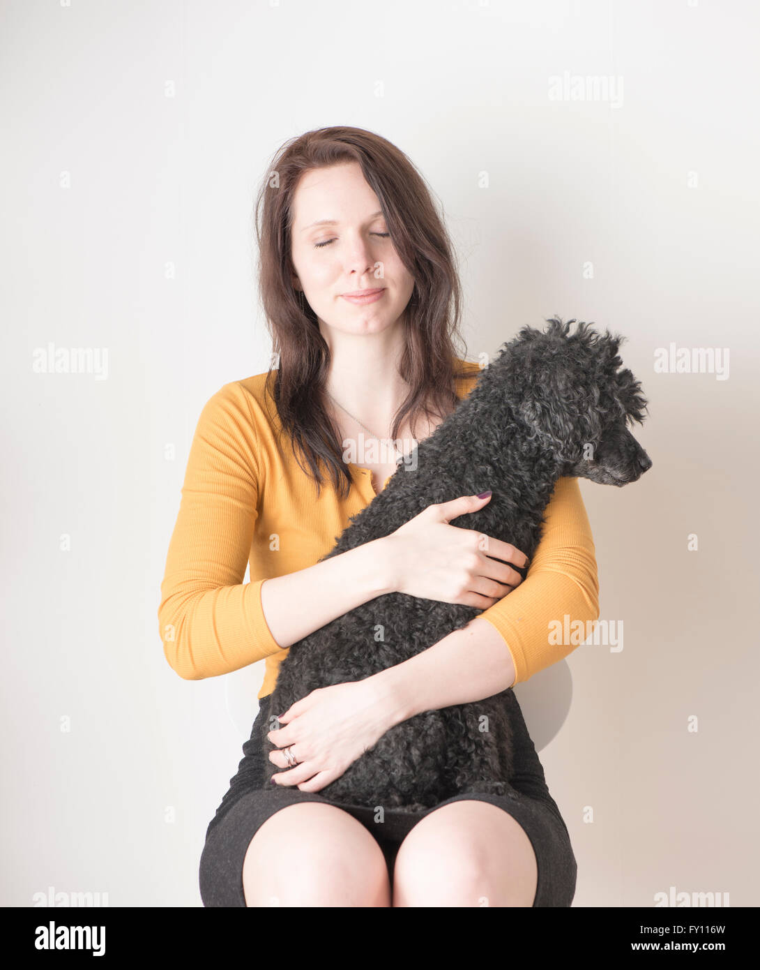 Frau mit Augen geschlossen halten schwarzen Pudel im Arm. Lifestyle-Bild zeigt Zuneigung und die Bindung zwischen Hund und Mensch. Stockfoto