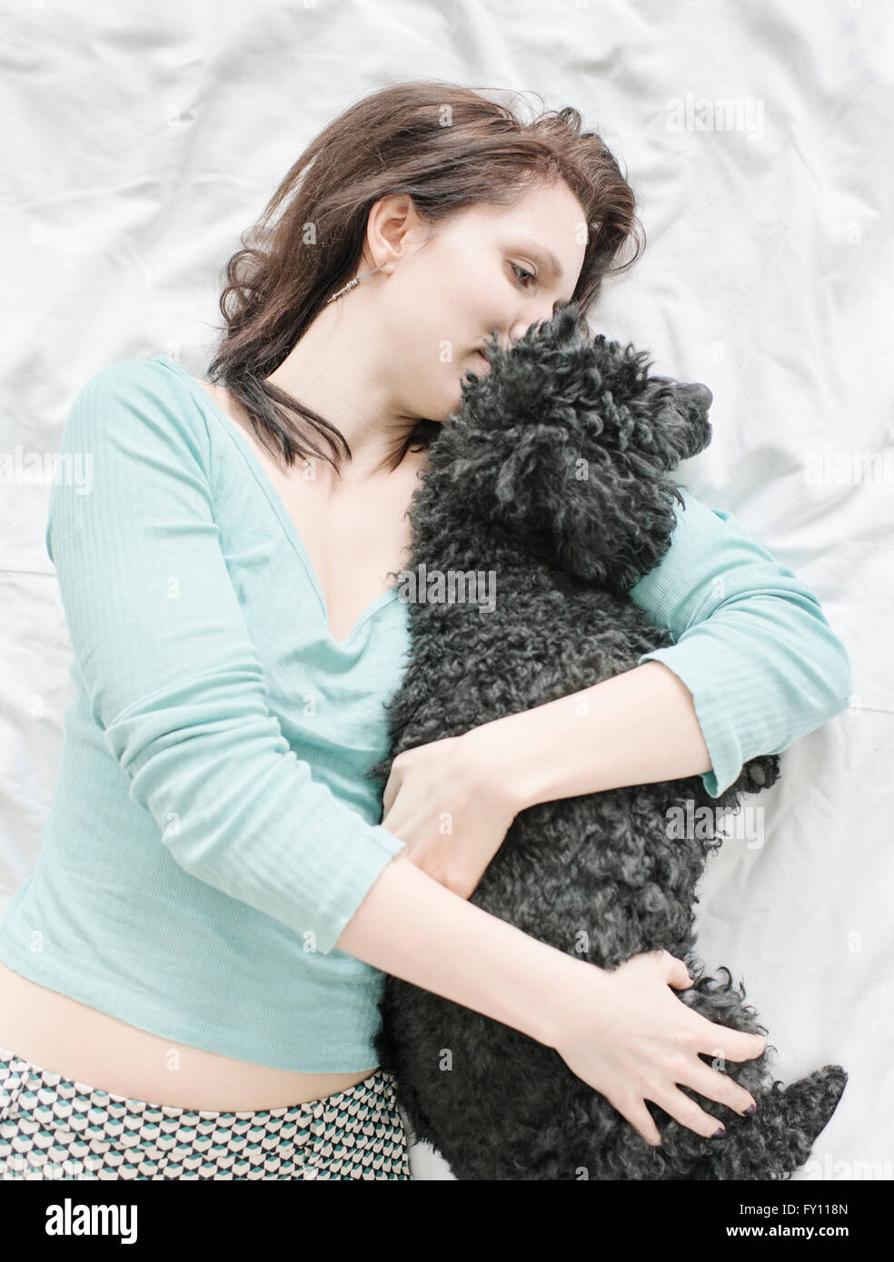 Frau liegend im Bett umarmt schwarzen Pudel. Lifestyle-Bild zeigt Zuneigung und die Bindung zwischen Hund und Mensch. Stockfoto