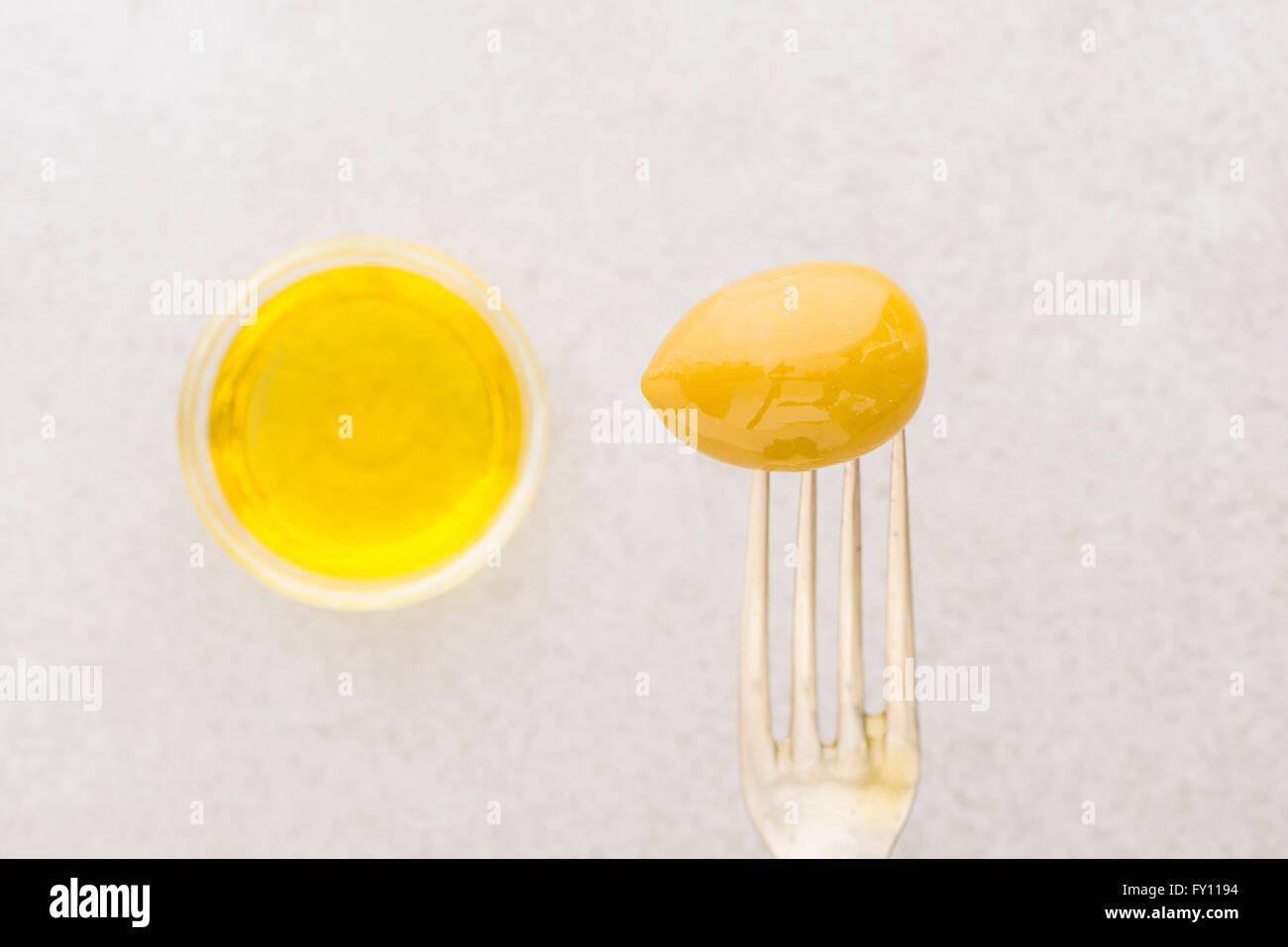 Eine grüne Olive auf Gabel und Olivenöl in Glasschale. Still-Leben Foto von Vorspeise oder Snack. Stockfoto