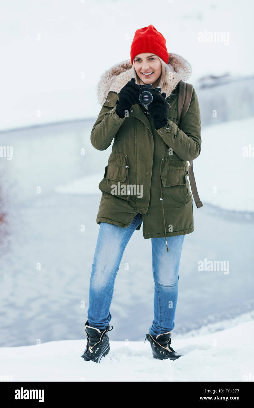 Schöne junge Frau, die im Winter durch Kamera fotografieren Stockfoto