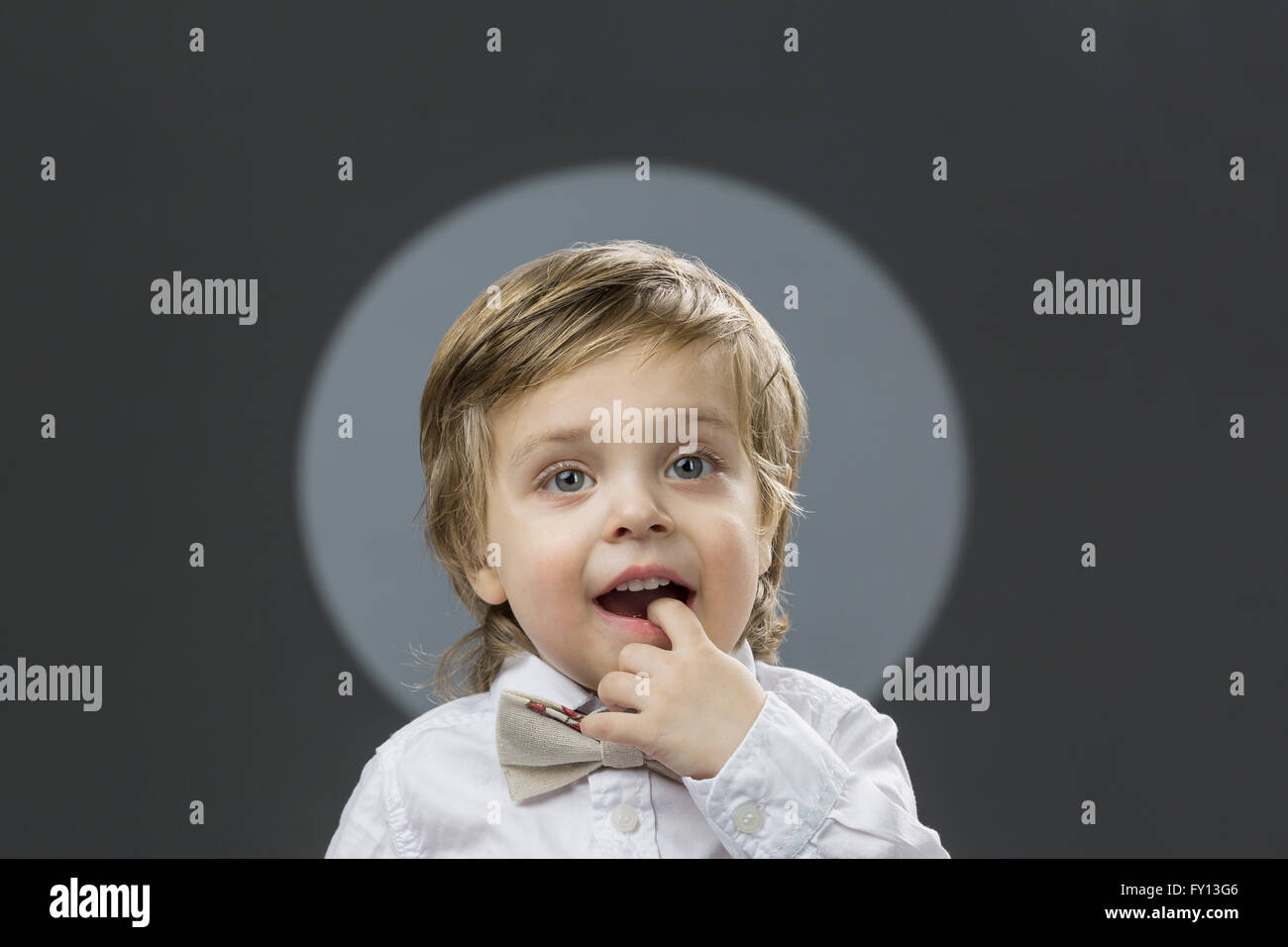 Porträt von süsser Boy mit Finger im Mund vor grauem Hintergrund Stockfoto