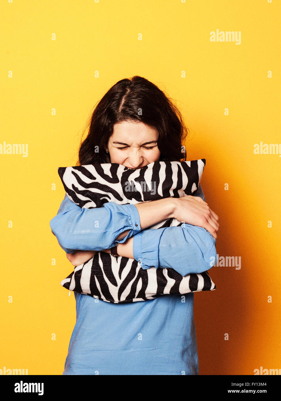 Gereizte junge Frau umarmt Kissen vor gelbem Hintergrund Stockfoto