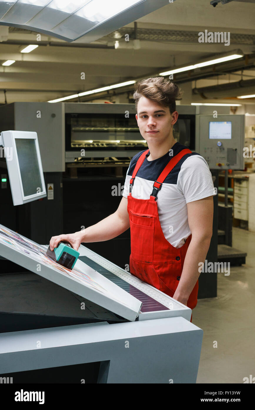 Porträt der jungen Arbeitnehmer hält Scanner über Ausdruck mit Maschinen an Druckmaschine Stockfoto