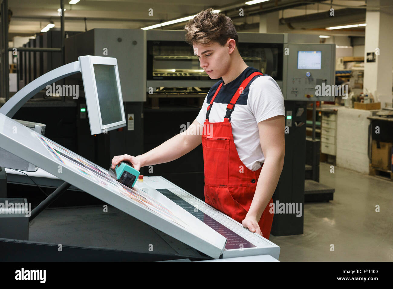 Junge Arbeitnehmer, die Qualitätsprüfung des Ausdrucks mit Maschinen an Druckmaschine zu tun Stockfoto
