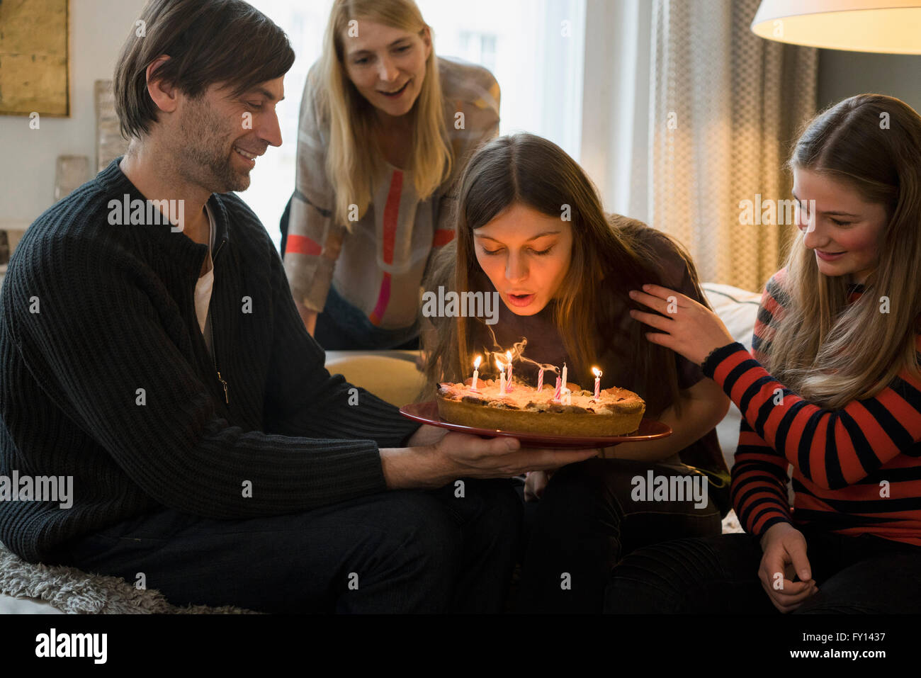 Familie sucht junge Frau bläst Geburtstagskerzen zu Hause Stockfoto