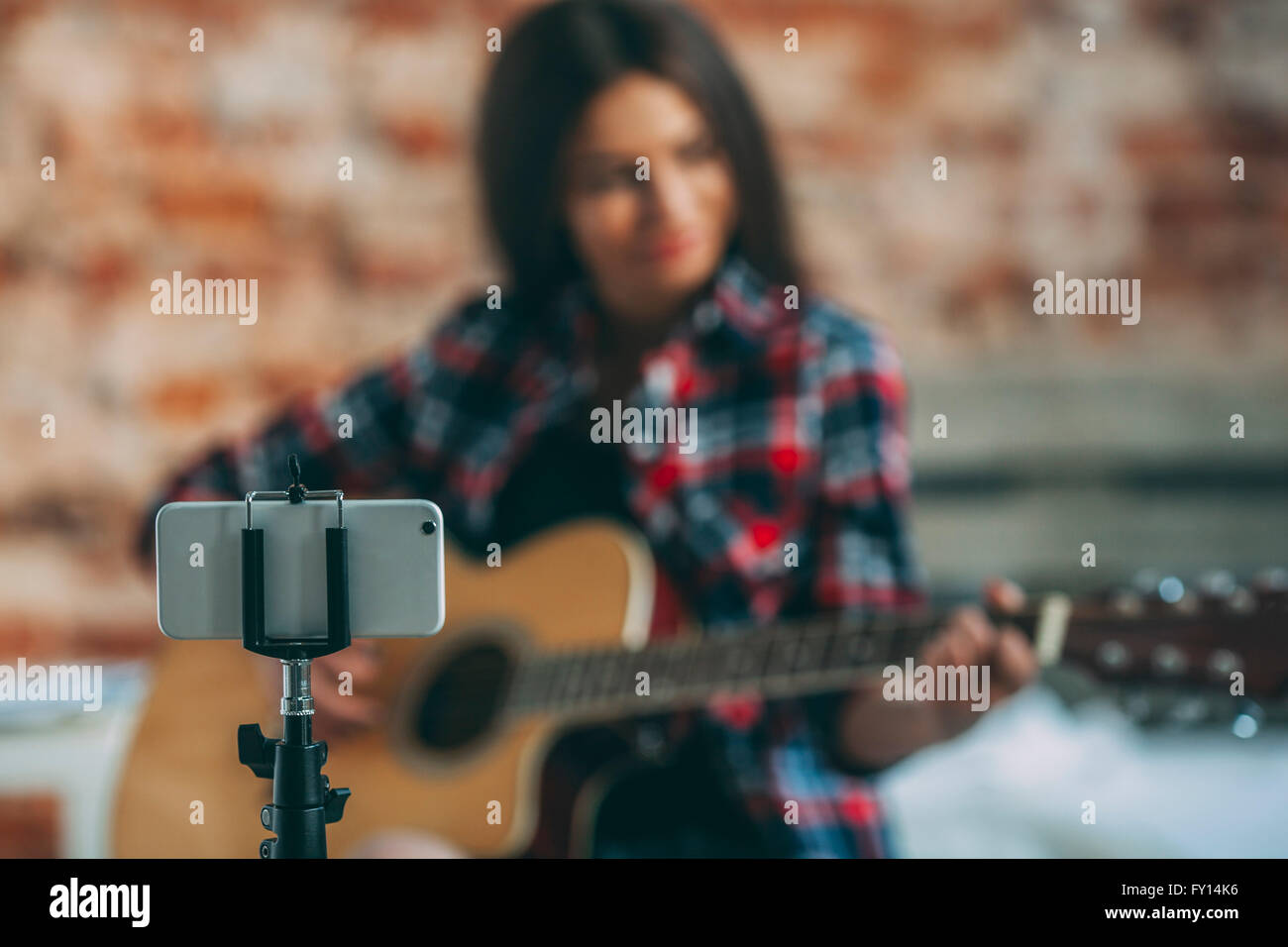 Smartphone in Einbeinstativ mit Frau spielt Gitarre im Hintergrund zu Hause Stockfoto