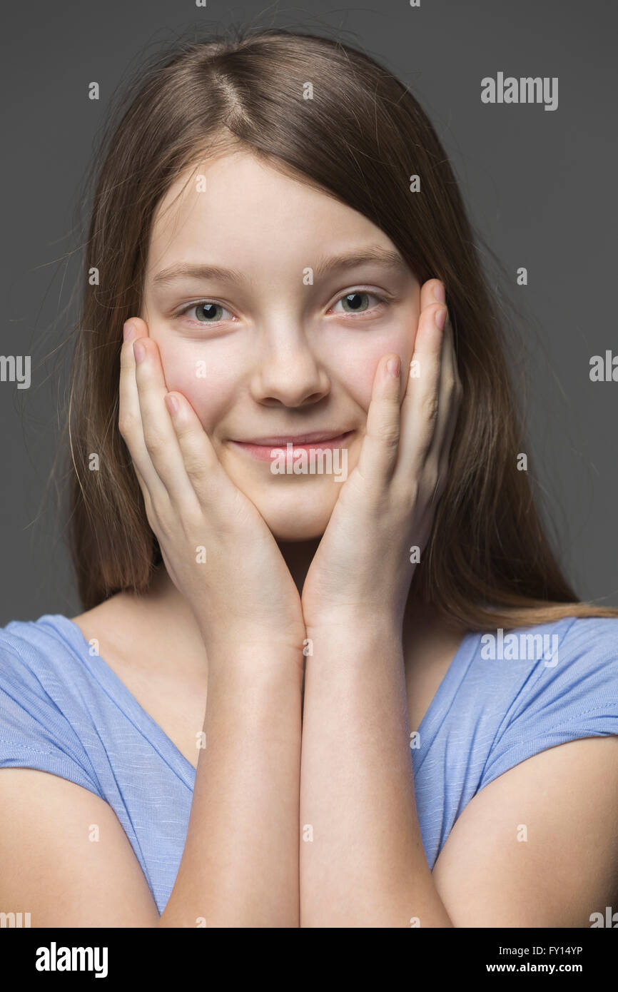 Close-up Portrait von lächelndes Mädchen mit Kopf in Händen vor grauem Hintergrund Stockfoto