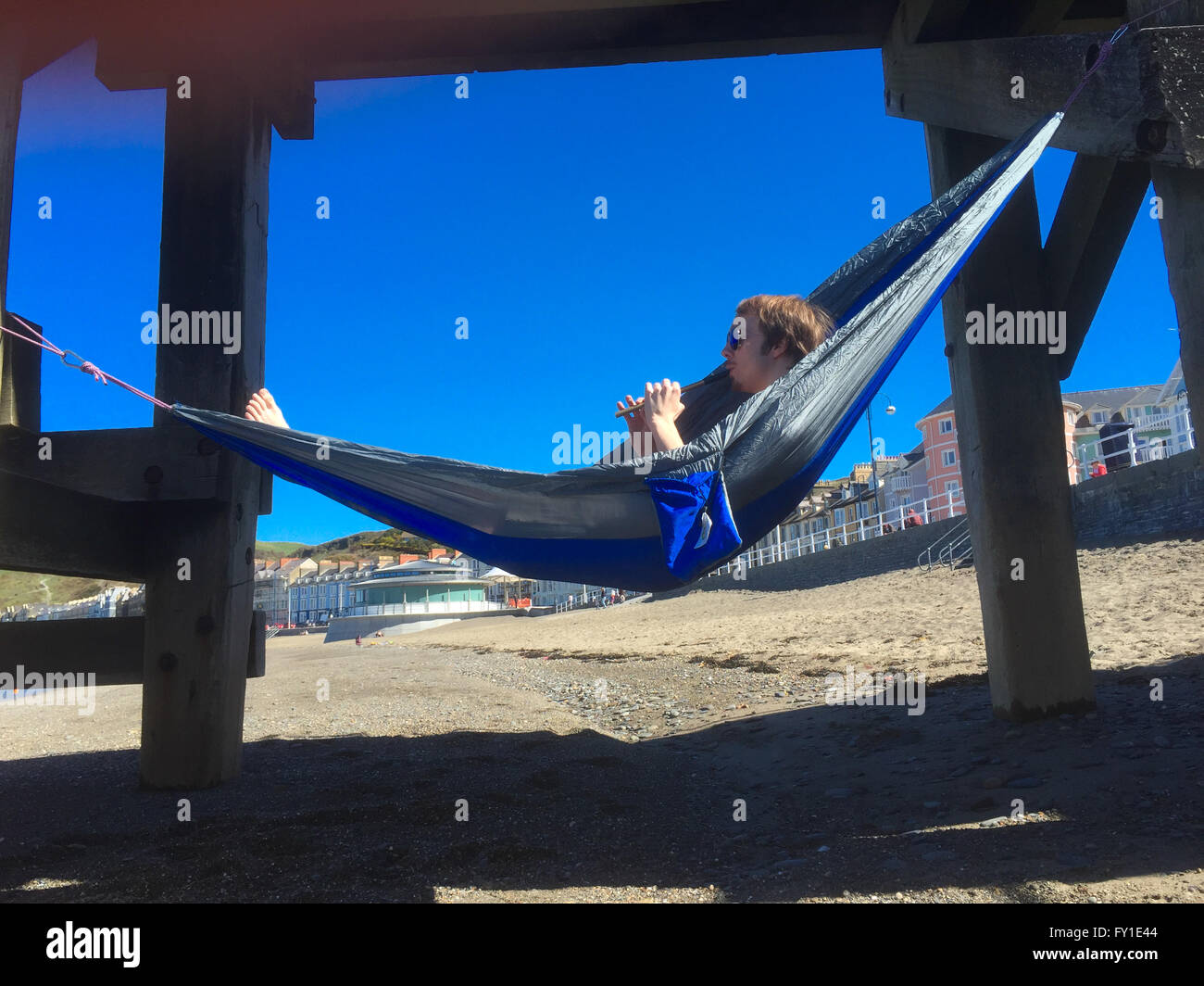 Aberystwyth Wales UK, Mittwoch, 20. April 2016 UK Wetter: ein Hochdrucksystem über das Vereinigte Königreich produziert täglich Sonnenschein in Aberystwyth, Wales, mit der Temperatur 18ºc in Teilen von Wales und den West Midlands zu erreichen.  Ein Student nimmt sich eine Auszeit vom Studium und entspannt in der Hängematte aufgehängt über den Strand in Aberystwyth Photo Credit: Keith Morris / Alamy Live News Stockfoto