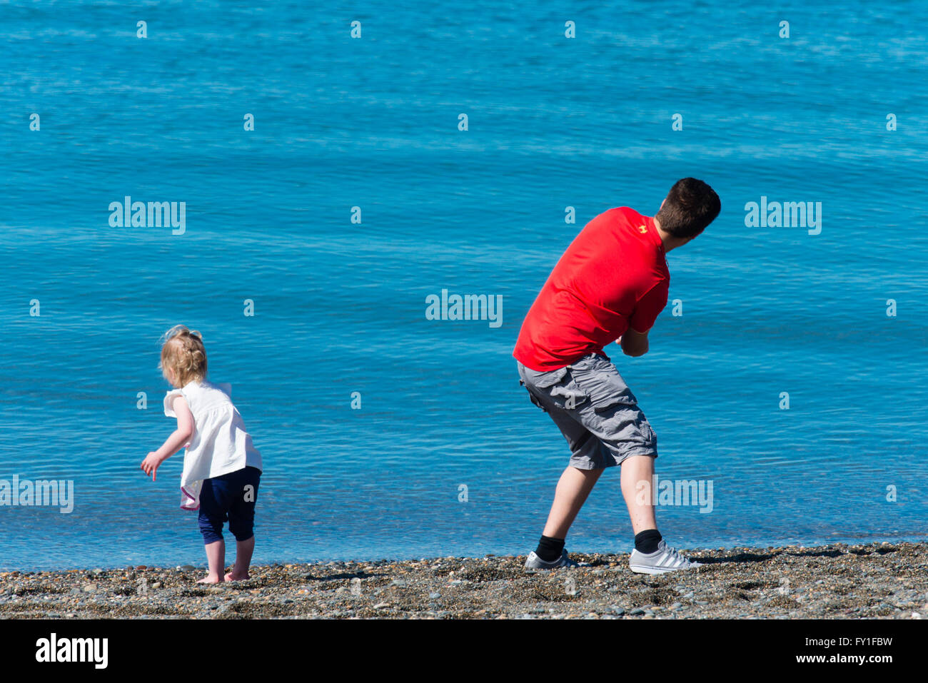 Aberystwyth Wales UK, Mittwoch, 20. April 2016 UK Wetter: ein Hochdrucksystem über das Vereinigte Königreich produziert täglich Sonnenschein in Aberystwyth, Wales, mit der Temperatur 18ºc in Teilen von Wales und den West Midlands zu erreichen.  Ein junger Vater spielt mit seiner Tochter, werfen Kieselsteine in ruhiger See Photo Credit: Keith Morris / Alamy Live News Stockfoto
