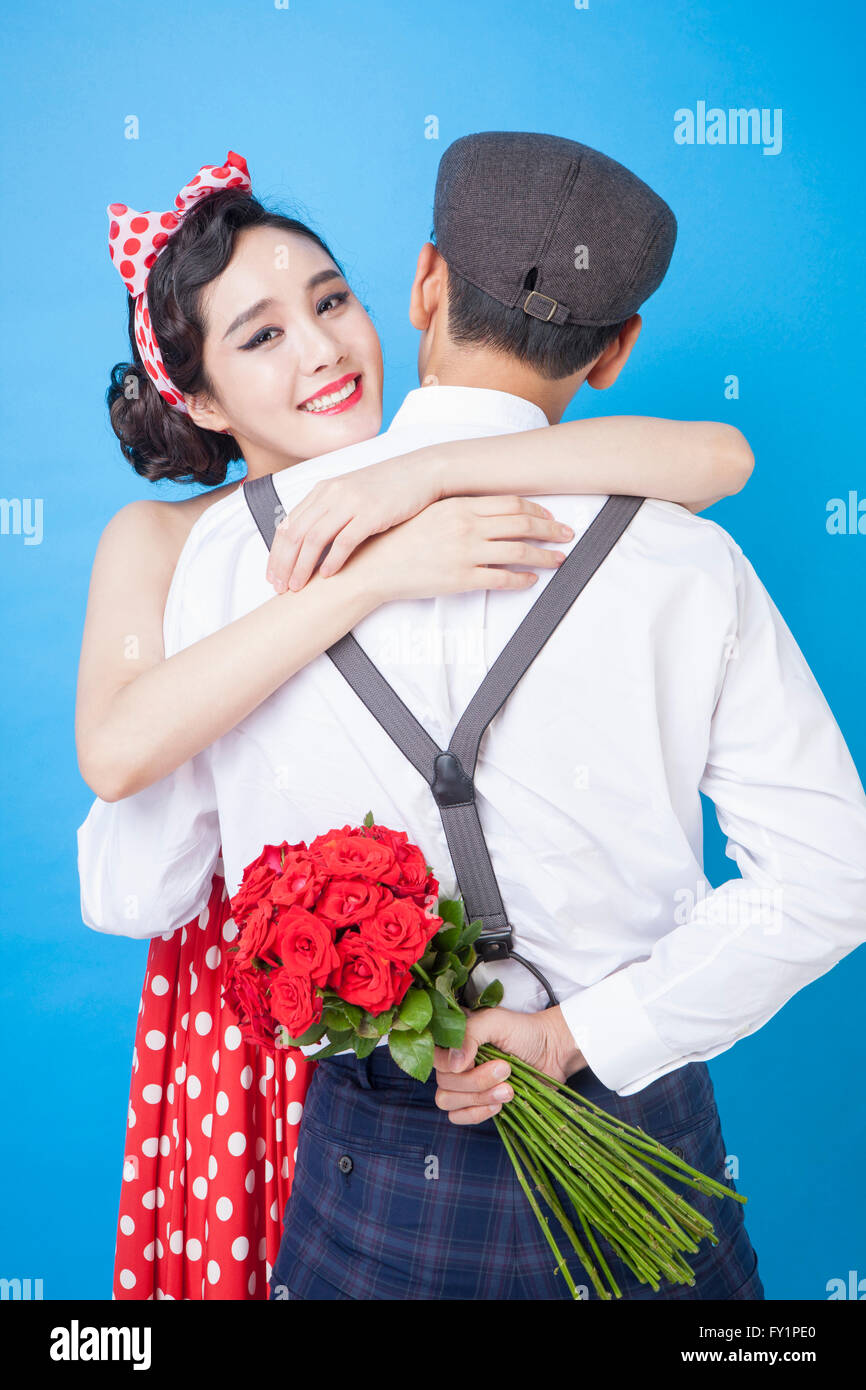 Junge lächelnde Frau im Retro-Stil, einen Mann mit einem Strauß roter Rosen auf seinem Rücken umarmt Stockfoto