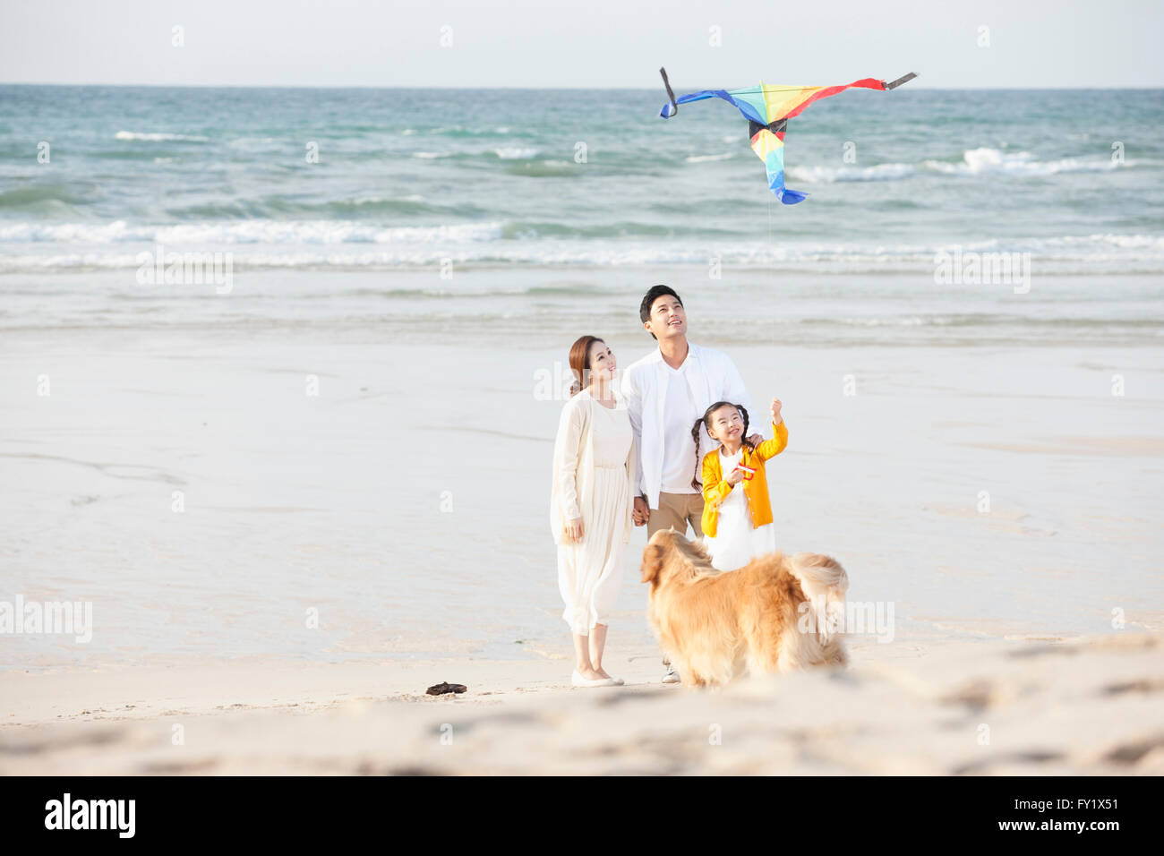 Mädchen fliegen einen Drachen und ihre Eltern am Strand mit einem Hund zusammen Stockfoto