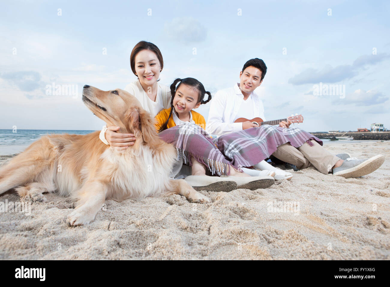 Familie mit einem Hund, glücklich und sitzen auf den Sandstrand in Jeju mit einem Lächeln Stockfoto