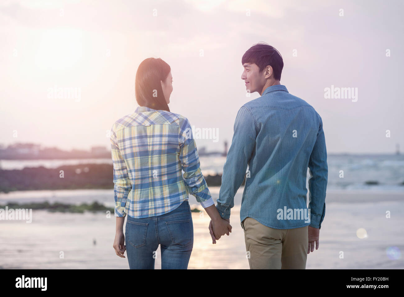 Paar Hand in hand sahen einander mit einem Lächeln am Strand Stockfoto