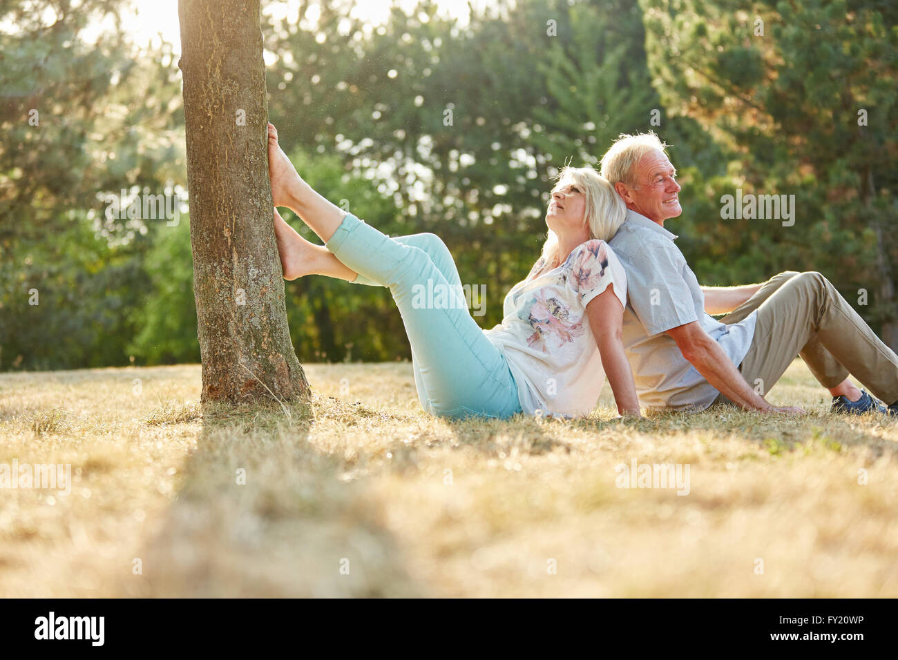 Älteres Paar in Liebe sitzen Rücken an Rücken auf dem Rasen im park Stockfoto