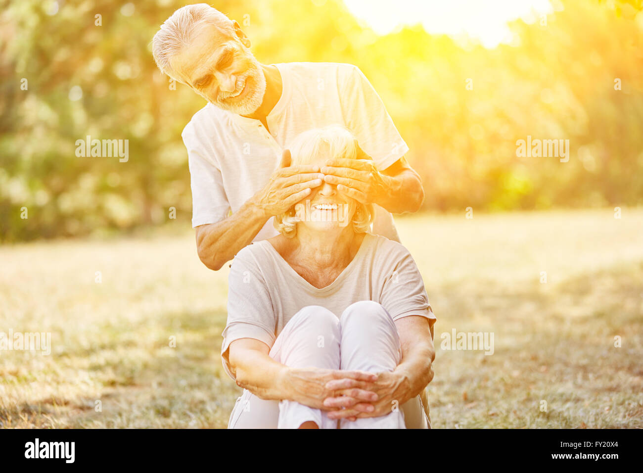 Alter Mann deckt lächelnde Frau Augen im Sommer im Garten Stockfoto