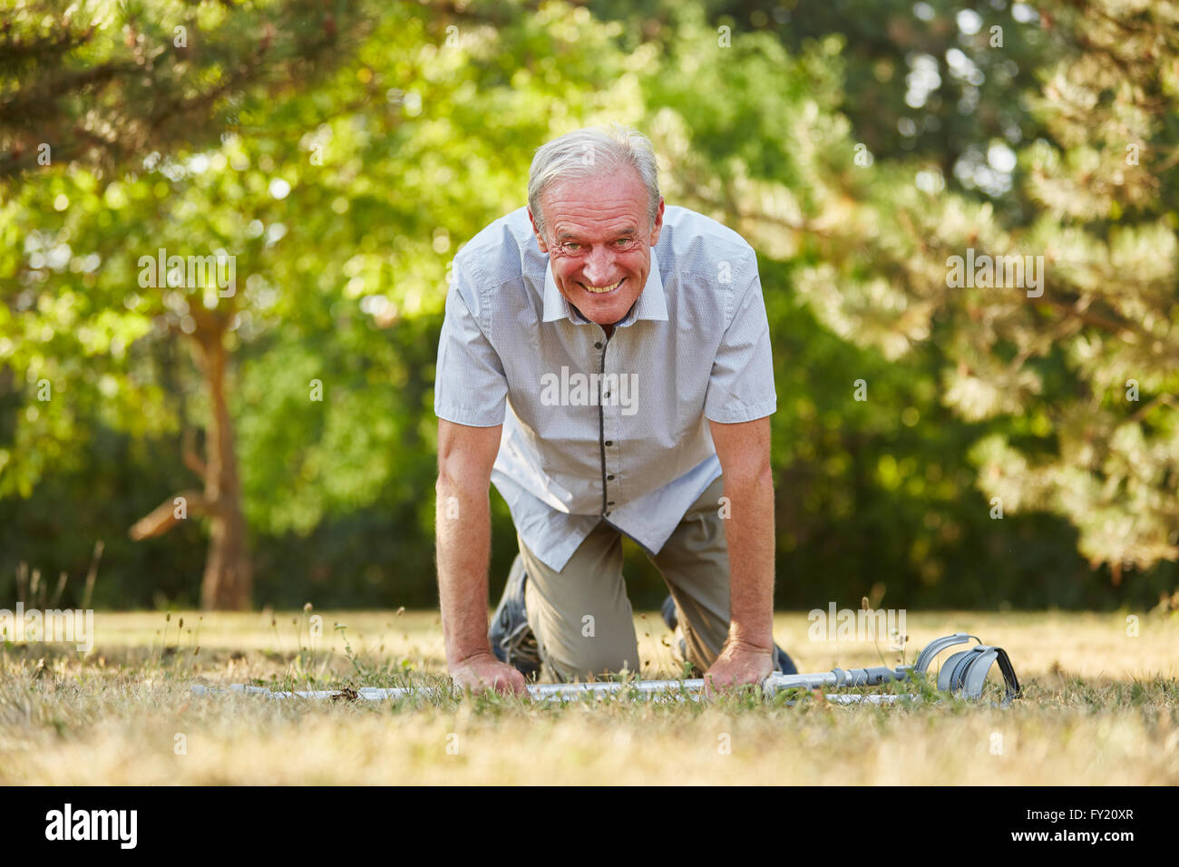 Alter Mann auf Krücken auf den Knien in der Natur im Sommer Spaß Stockfoto