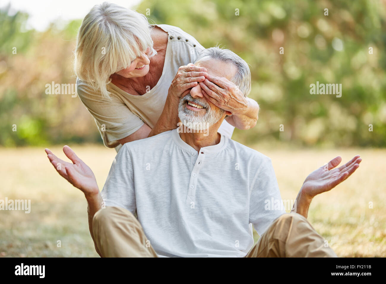 Alte Frau bedeckt ihres Mannes Augen von der Rückseite im Sommer in der Natur Stockfoto