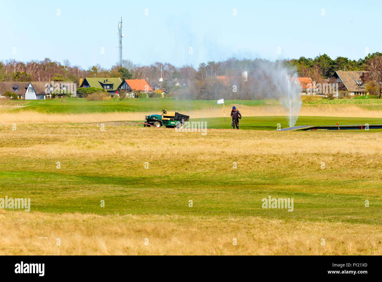 Skanor, Schweden - 11. April 2016: Männliche Arbeiter auf dem Golfplatz Bewässerung ist aber der Wasserschlauch ist undicht und verbreiten Sie Wasser in Stockfoto
