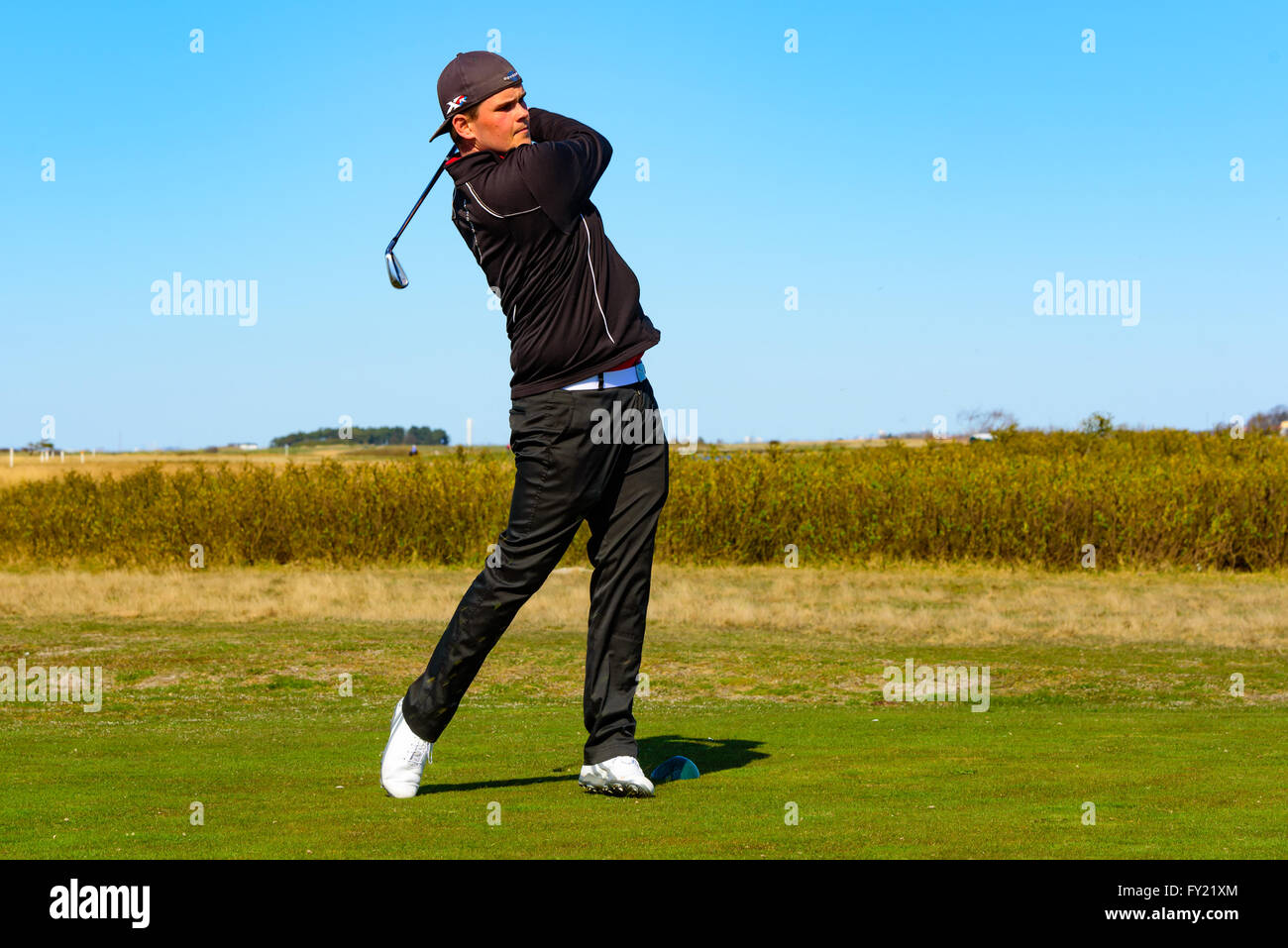 Skanor, Schweden - 11 April 2016: Männliche junge Erwachsene Golfspieler am Ende seiner Schwingen. Er ist ganz in schwarz gekleidet und tragen eine Kappe. Stockfoto