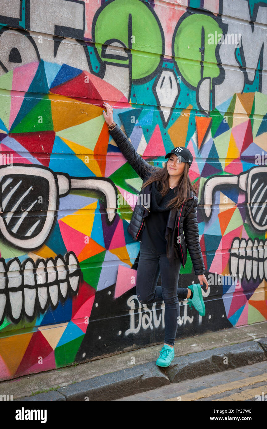 Ein Tourist posiert vor einigen Straßenkunst in Grimsby Street East London E2 durch D Screet - RIP Lee Muz Stockfoto