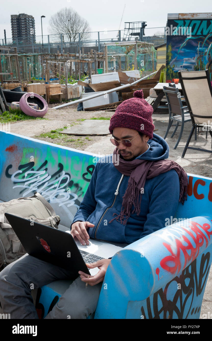 Ein junger Mann in Wollmütze arbeiten am Laptop in die Nomadic Community Gardens in Tower Hamlets Stockfoto