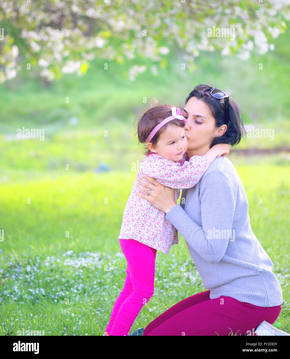 Familie, Kinder und glückliche Menschen Konzept - glückliches kleines Mädchen umarmen und küssen ihre Mutter auf grünem Hintergrund Stockfoto