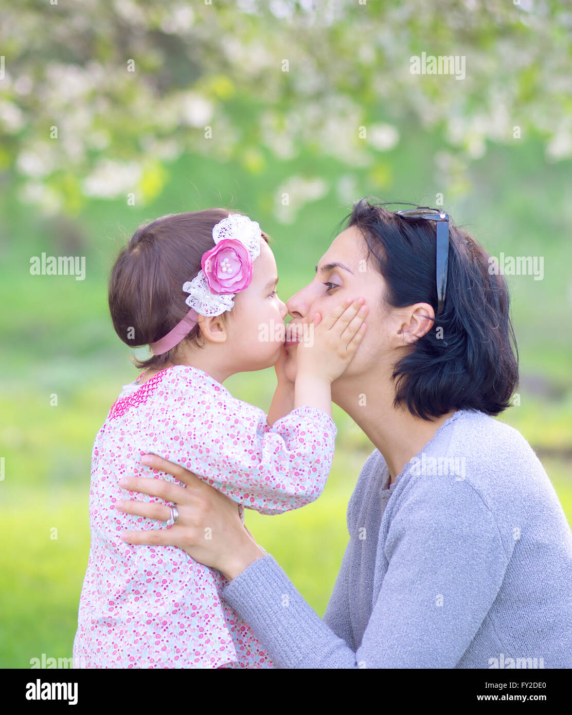Familie, Kinder und glückliche Menschen Konzept - glückliches kleines Mädchen umarmen und küssen ihre Mutter auf grünem Hintergrund Stockfoto