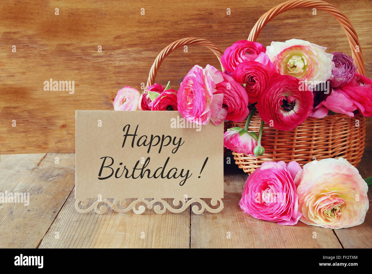 Rosa Blumen im Korb neben Karte mit Satz: alles Gute zum Geburtstag, am Holztisch. Stockfoto