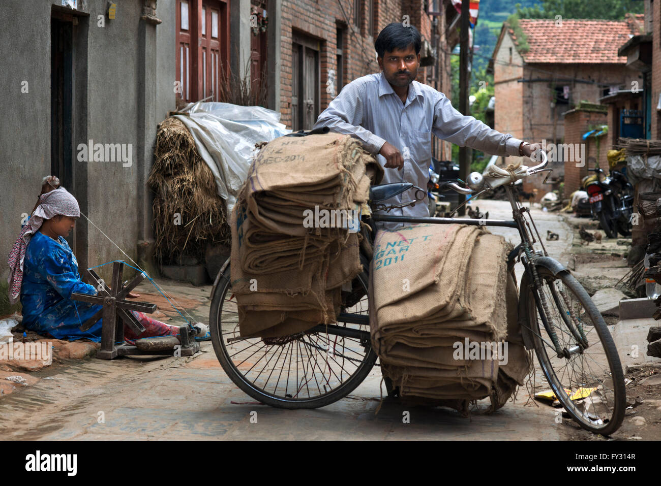 Ein Mann mit einem alten Fahrrad und eine Frau spinnt Wolle in dem kleinen Dorf Bungamati, Nepal Stockfoto