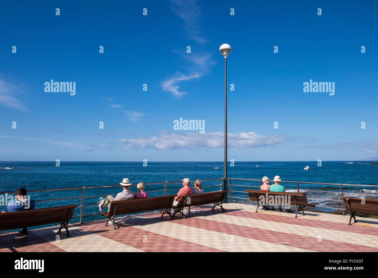 Besucher sitzen und entspannen auf den Bänken am Aussichtspunkt Mirador an der Küste von La Caleta, Costa Adeje, Teneriffa, Kanarische Islan Stockfoto