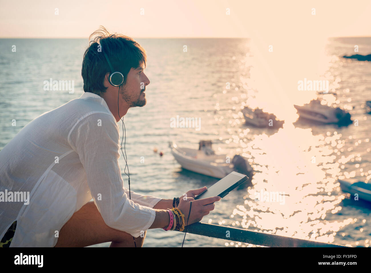 Kerl Musik hören mit Kopfhörern aus Tablet in einer Ferien-Destination in der Nähe von Booten Stockfoto