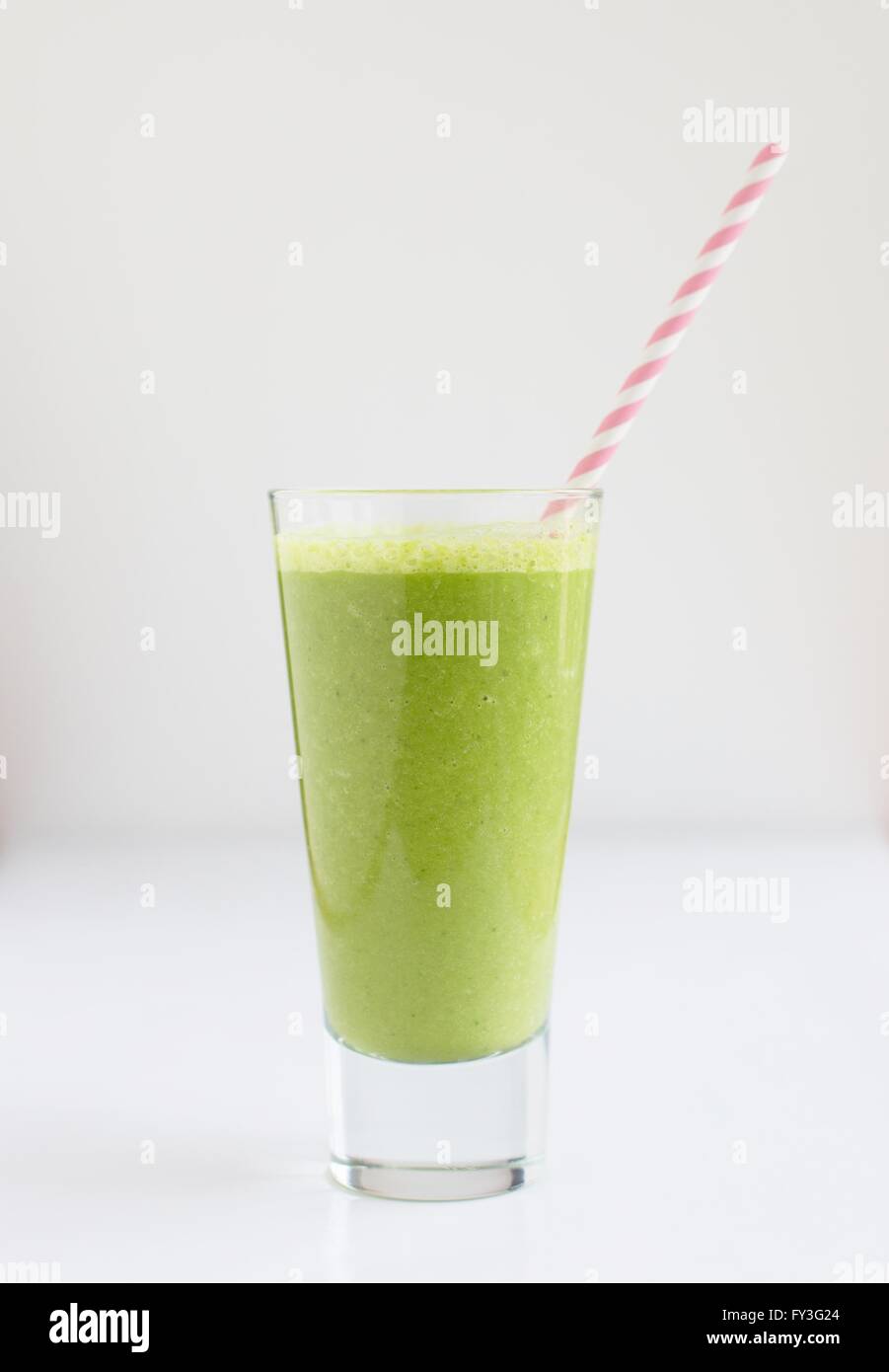 Ein grüner Smoothie Drink in ein Glas mit einem rosa-weiß gestreiften Strohhalm. Stockfoto